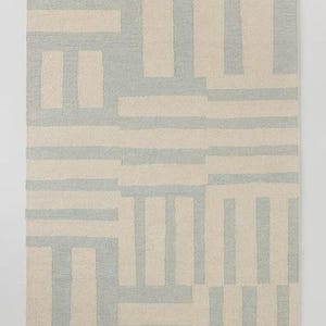 May include: Rectangular area rug with a geometric pattern. The rug features a repeating design of light blue and beige rectangular shapes. The pattern is a mix of horizontal and vertical lines, creating a modern, abstract look. The rug is made of a woven material.