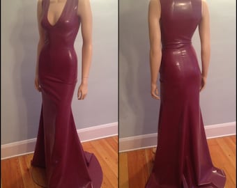 Puede incluir: Un vestido largo de látex burdeos sin mangas, con escote en V y un corpiño ajustado. El vestido tiene una falda de estilo sirena que se ensancha en la parte inferior.