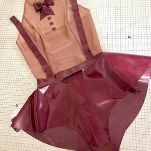 Może przedstawiać: Spódnica z lateksu w kolorze bordowym z przezroczystą, cielesną górą z lateksu z muszką. Góra ma ramiączka i zapięcie na guziki.