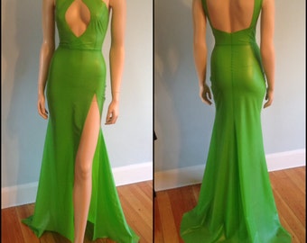 May include: A bright green, form-fitting, sleeveless gown with a plunging neckline and a thigh-high slit. The gown has a mermaid-style skirt and a criss-cross detail at the bodice.