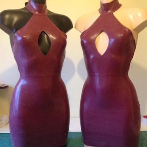 Puede incluir: Dos vestidos de látex burdeos exhibidos en maniquíes. Los vestidos presentan un cuello halter, un detalle de ojo de cerradura en el pecho y una silueta ajustada. Los maniquíes tienen diferentes tonos de piel, uno negro y otro beige.