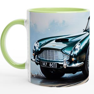 以下が含まれることがあります： 緑色のハンドルと内側を備えた白いセラミックマグ。マグには、クラシックな緑色のスポーツカーの詳細なイラストが描かれています。車にはクロムグリルがあり、ナンバープレートには「IA7 6011」と書かれています。