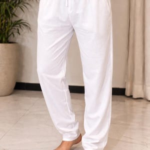 May include: White drawstring pants with pockets. The pants are made of a lightweight fabric and have a relaxed fit. The model is wearing the pants with a white top. The pants are suitable for casual wear.