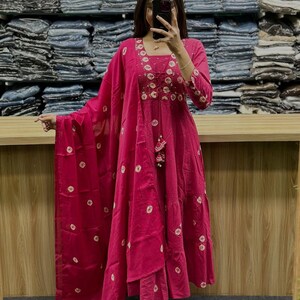 May include: A magenta-colored Indian salwar kameez suit with white circular patterns. The suit features intricate embroidery around the neckline and sleeves. The outfit includes a matching dupatta and pants, creating a coordinated ensemble.