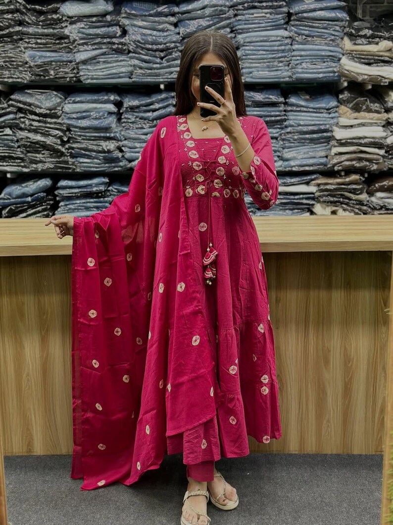 May include: A magenta-colored Indian salwar kameez suit with white circular patterns. The suit features intricate embroidery around the neckline and sleeves. The outfit includes a matching dupatta and pants, creating a coordinated ensemble.