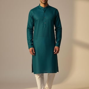 May include: A teal kurta with a mandarin collar and long sleeves, worn with off-white trousers. The kurta features a button-down front and side slits. The outfit is completed with brown sandals. The clothing is likely made of a lightweight fabric.