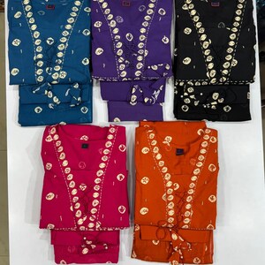 May include: Five sets of matching pajamas in various colors: teal, purple, black, hot pink, and orange. Each set features a top with a lace-up neckline and a repeating white circular pattern, paired with matching pants.