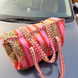 May include: A striped duffel bag with a zip. The bag has alternating vertical stripes of pink and red, with tiger print accents. The handles are red and white striped.