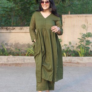 Peut inclure: Ensemble vert olive compos&eacute; d'une robe et d'un pantalon assorti. La robe a un col en V, des manches longues et une fermeture boutonn&eacute;e sur le devant. Le pantalon est coup&eacute; &agrave; la cheville. La personne porte des lunettes de soleil et des boucles d'oreilles.