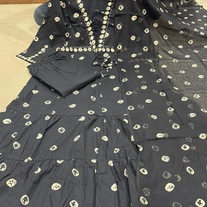 May include: A black two-piece outfit featuring a long-sleeved top and matching pants. The top has a decorative neckline and a tiered skirt. The fabric is adorned with a repeating pattern of white circular designs. The outfit is made of a lightweight material.