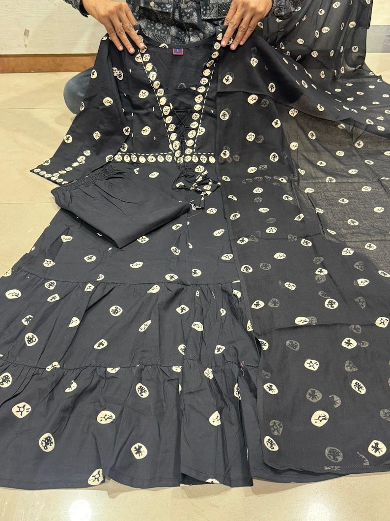 May include: A black two-piece outfit featuring a long-sleeved top and matching pants. The top has a decorative neckline and a tiered skirt. The fabric is adorned with a repeating pattern of white circular designs. The outfit is made of a lightweight material.