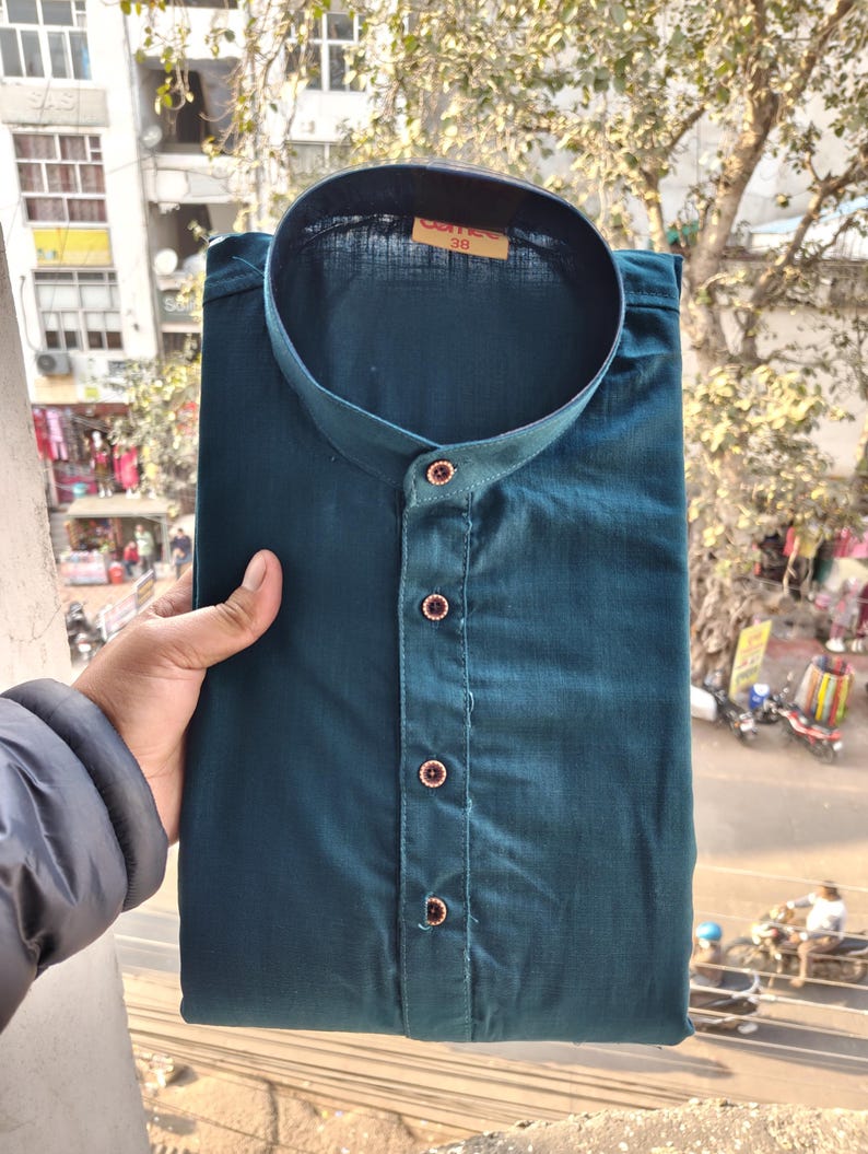 May include: Teal button-down shirt with a mandarin collar. The shirt is folded and appears to be made of a soft fabric. The buttons are a contrasting colour. The tag on the collar reads "38".