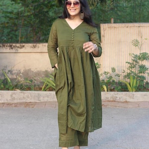 Peut inclure: Ensemble vert olive compos&eacute; d'une robe et d'un pantalon assorti. La robe a un col en V, des manches longues et une fermeture boutonn&eacute;e sur le devant. Le pantalon est coup&eacute; &agrave; la cheville. La personne porte des lunettes de soleil et des boucles d'oreilles.