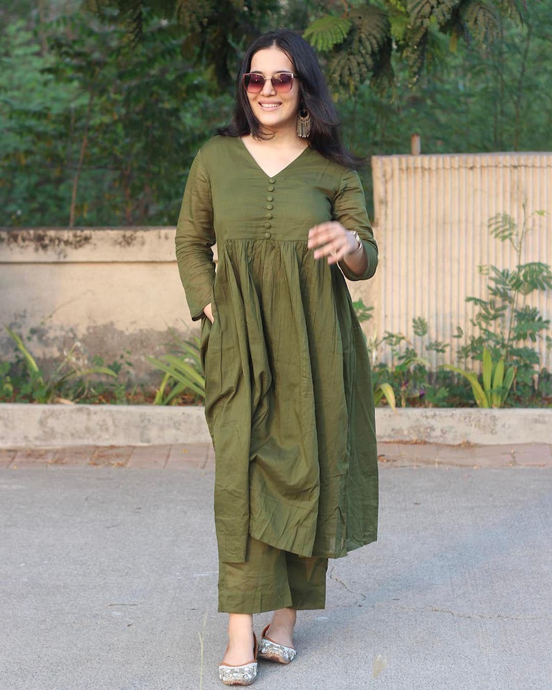 Peut inclure: Ensemble vert olive compos&eacute; d'une robe et d'un pantalon assorti. La robe a un col en V, des manches longues et une fermeture boutonn&eacute;e sur le devant. Le pantalon est coup&eacute; &agrave; la cheville. La personne porte des lunettes de soleil et des boucles d'oreilles.