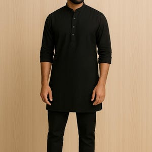 Puede incluir: Una t&uacute;nica negra con cuello mandar&iacute;n y tapeta abotonada, combinada con pantalones negros a juego. El conjunto se completa con sandalias de cuero marr&oacute;n. La ropa es probablemente parte de un atuendo tradicional o cultural.