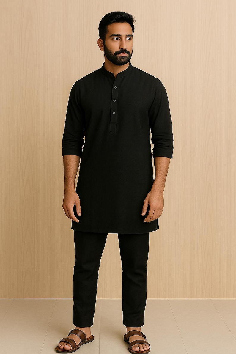 Puede incluir: Una t&uacute;nica negra con cuello mandar&iacute;n y tapeta abotonada, combinada con pantalones negros a juego. El conjunto se completa con sandalias de cuero marr&oacute;n. La ropa es probablemente parte de un atuendo tradicional o cultural.