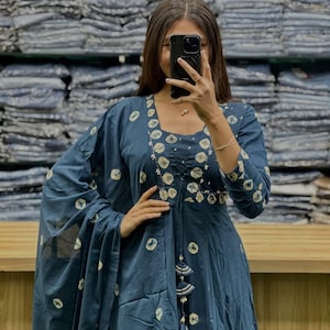 May include: A dark blue dress with a matching shawl. The dress features a round neckline, long sleeves, and a flowing skirt. It is adorned with a white circular pattern. The shawl is draped over the shoulders.