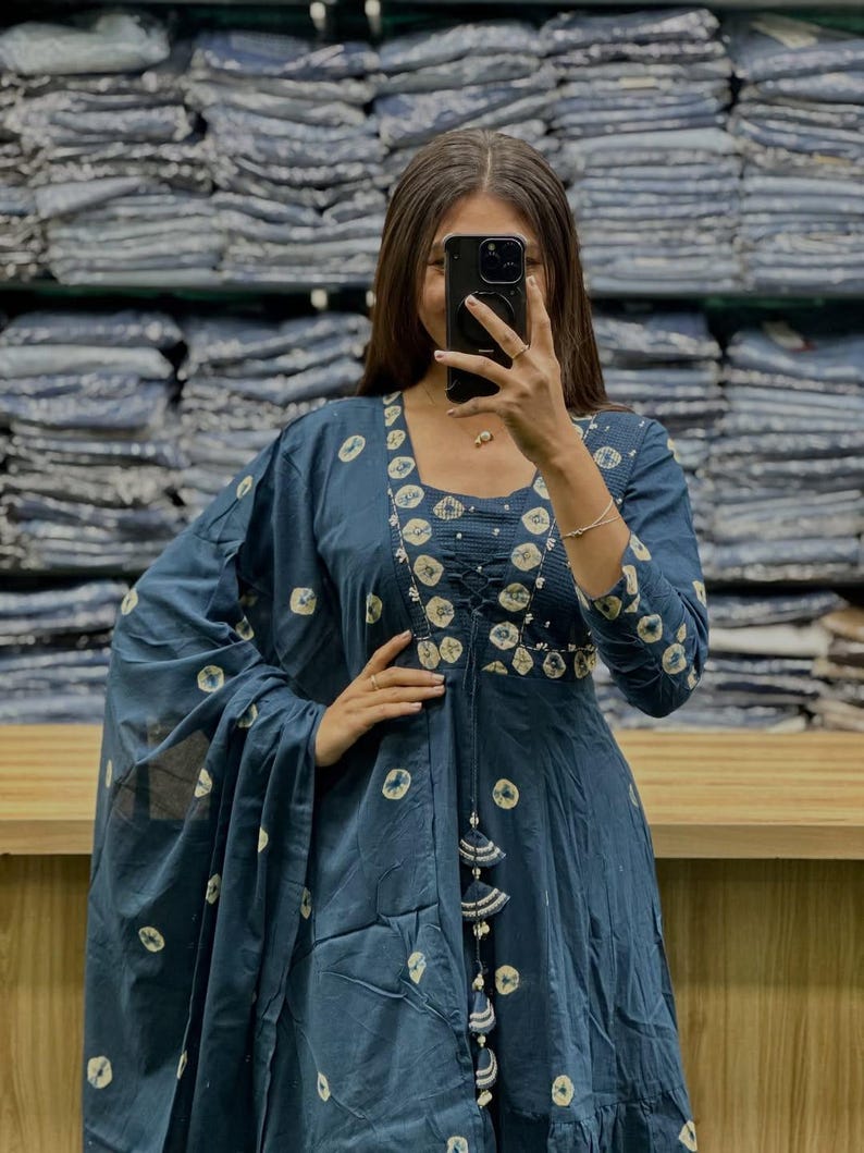 May include: A dark blue dress with a matching shawl. The dress features a round neckline, long sleeves, and a flowing skirt. It is adorned with a white circular pattern. The shawl is draped over the shoulders.