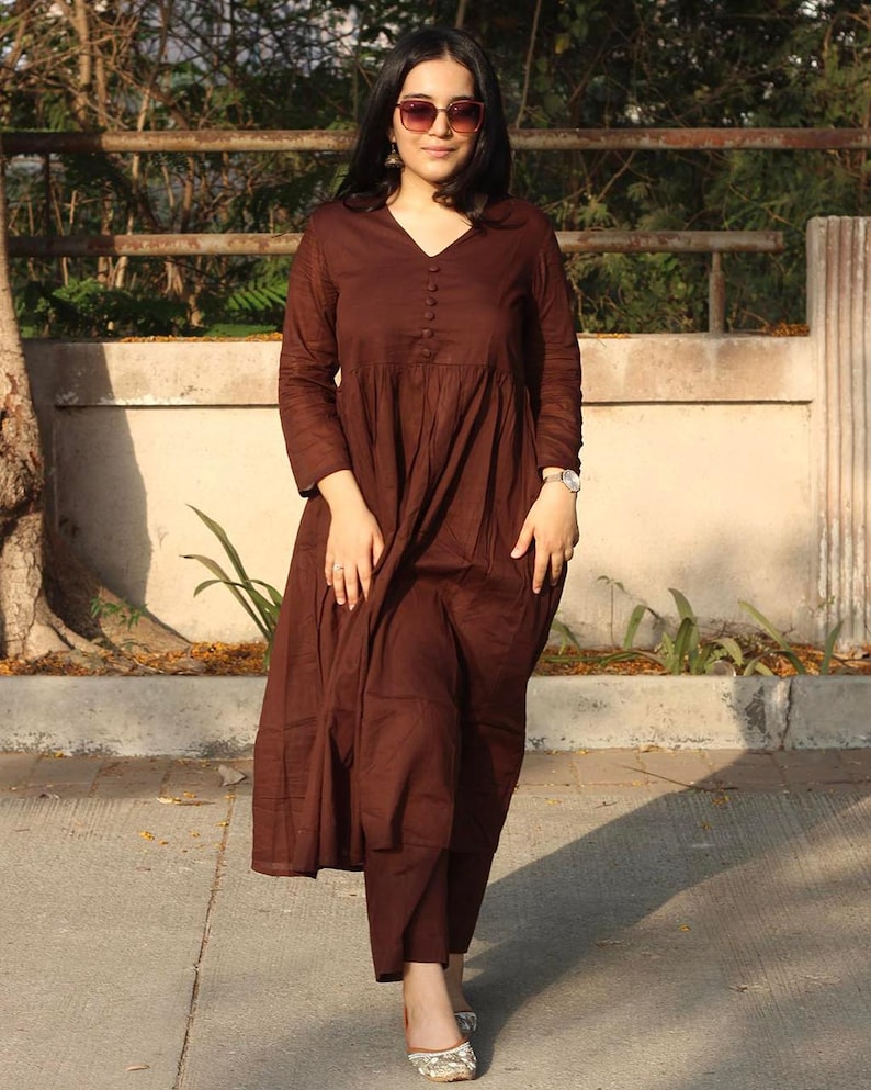 Peut inclure: Une robe marron &agrave; manches longues avec un col en V et des boutons. La robe a une jupe &eacute;vas&eacute;e et est associ&eacute;e &agrave; un pantalon assorti. La personne porte des lunettes de soleil et une montre. La tenue est adapt&eacute;e aux tenues d&eacute;contract&eacute;es.