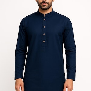 May include: Dark navy blue long-sleeved tunic with a mandarin collar and button-down front. The tunic has a straight hem and is made of a solid, dark blue fabric. The buttons are light brown.
