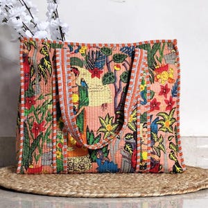 Puede incluir: Un bolso tote grande con un colorido diseño floral y de figuras. El bolso presenta un fondo melocotón con un patrón repetido de flores, árboles y personas. Las asas y el ribete son de color naranja con rayas blancas. El bolso está sobre una estera tejida.