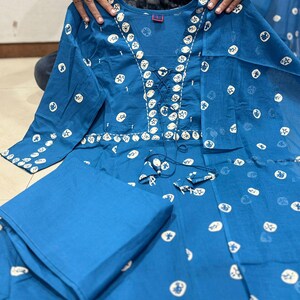 May include: A two-piece teal outfit featuring a long-sleeved top and matching pants. The top has a round neckline and is adorned with white circular and star-shaped patterns. The top has a lace-up detail at the neckline.