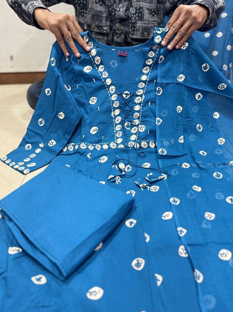 May include: A two-piece teal outfit featuring a long-sleeved top and matching pants. The top has a round neckline and is adorned with white circular and star-shaped patterns. The top has a lace-up detail at the neckline.