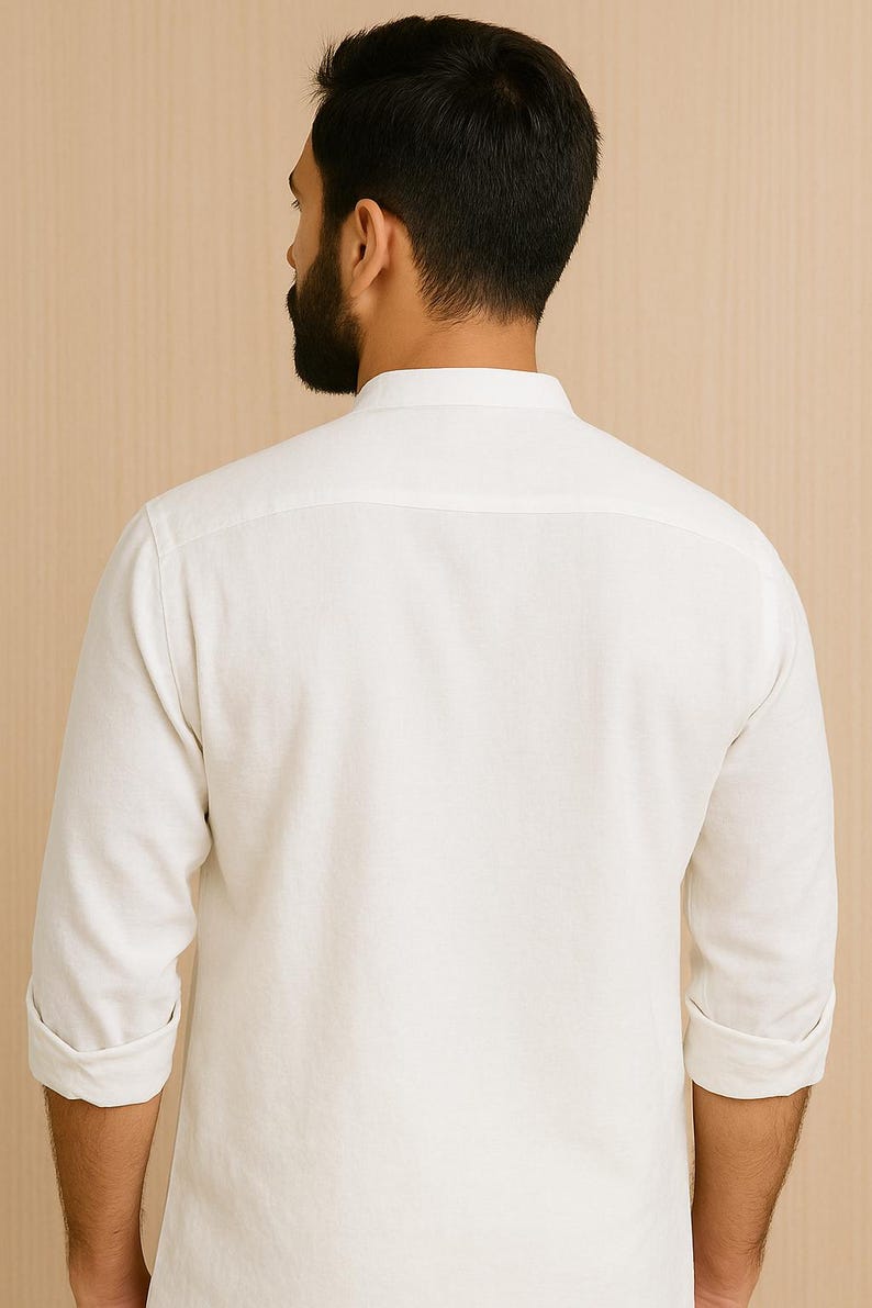Pu&ograve; includere: Una camicia bianca a maniche lunghe con colletto alla coreana. Le maniche sono arrotolate all'altezza dei gomiti. La camicia &egrave; realizzata in un tessuto morbido e di colore chiaro. La schiena della camicia &egrave; visibile.