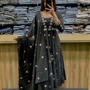 May include: Black long dress with white circular patterns and a matching shawl. The dress features a square neckline, three-quarter sleeves, and tiered skirt. The dress is accessorized with a tassel and is worn with sandals.