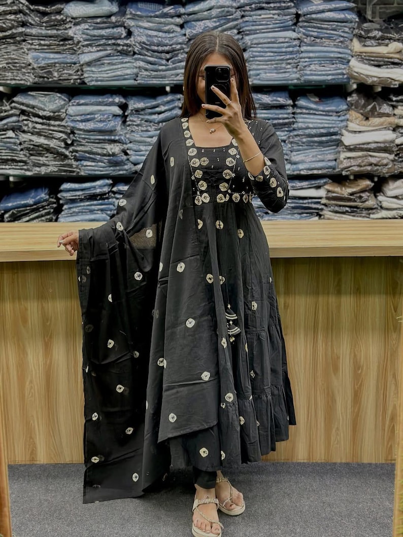 May include: Black long dress with white circular patterns and a matching shawl. The dress features a square neckline, three-quarter sleeves, and tiered skirt. The dress is accessorized with a tassel and is worn with sandals.