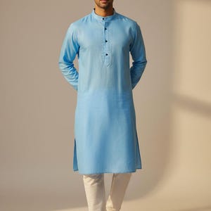 May include: A light blue kurta with a mandarin collar and long sleeves. The kurta features a button-down front and is worn with white trousers. This is a traditional Indian garment, suitable for casual or formal occasions.