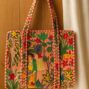 Könnte beinhalten: Gesteppte Tragetasche mit einem lebendigen Blumen- und Figuren-Design in Orange-, Grün- und Rottönen. Die Tasche hat eine rechteckige Form mit passenden orange-weiß gestreiften Griffen und Besatz. Die Tasche ist aus weichem, gestepptem Material.