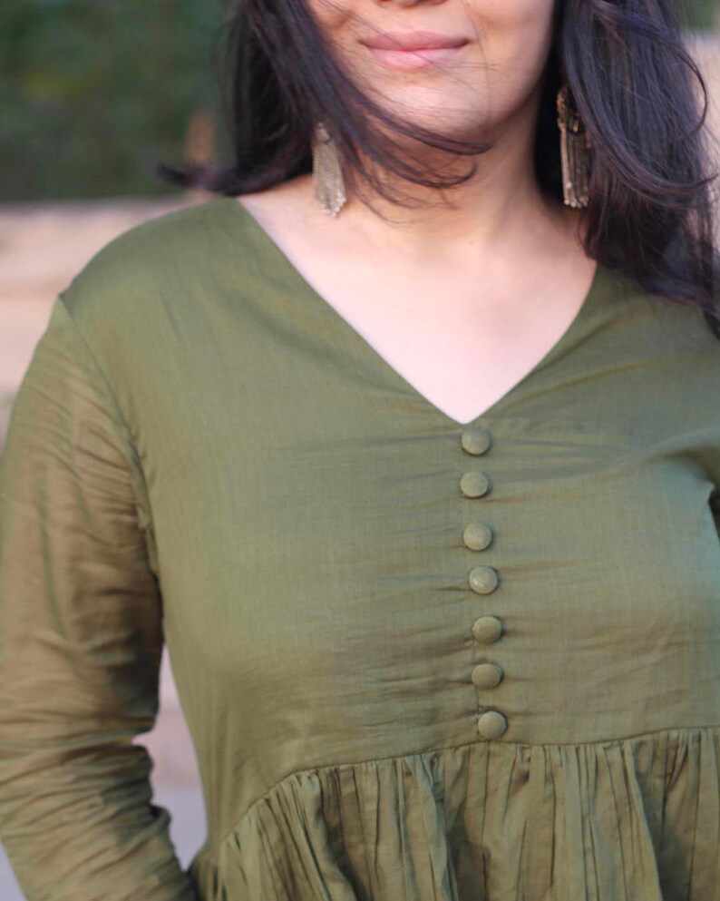 Peut inclure: Haut vert olive &agrave; manches longues avec un col en V et une rang&eacute;e de boutons assortis au centre. Le haut pr&eacute;sente un design fronc&eacute; et pliss&eacute; &agrave; la taille et est fait d'un tissu l&eacute;ger. Les manches sont longues et l&eacute;g&egrave;rement transparentes.