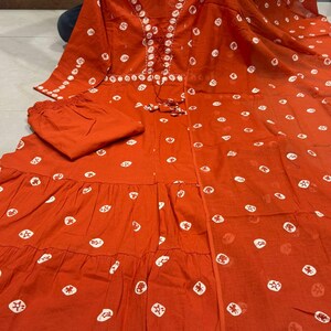 May include: A two-piece orange outfit with white polka dot patterns. The top has a V-neck with white embroidery and a drawstring. The outfit includes matching pants. The fabric appears to be lightweight.