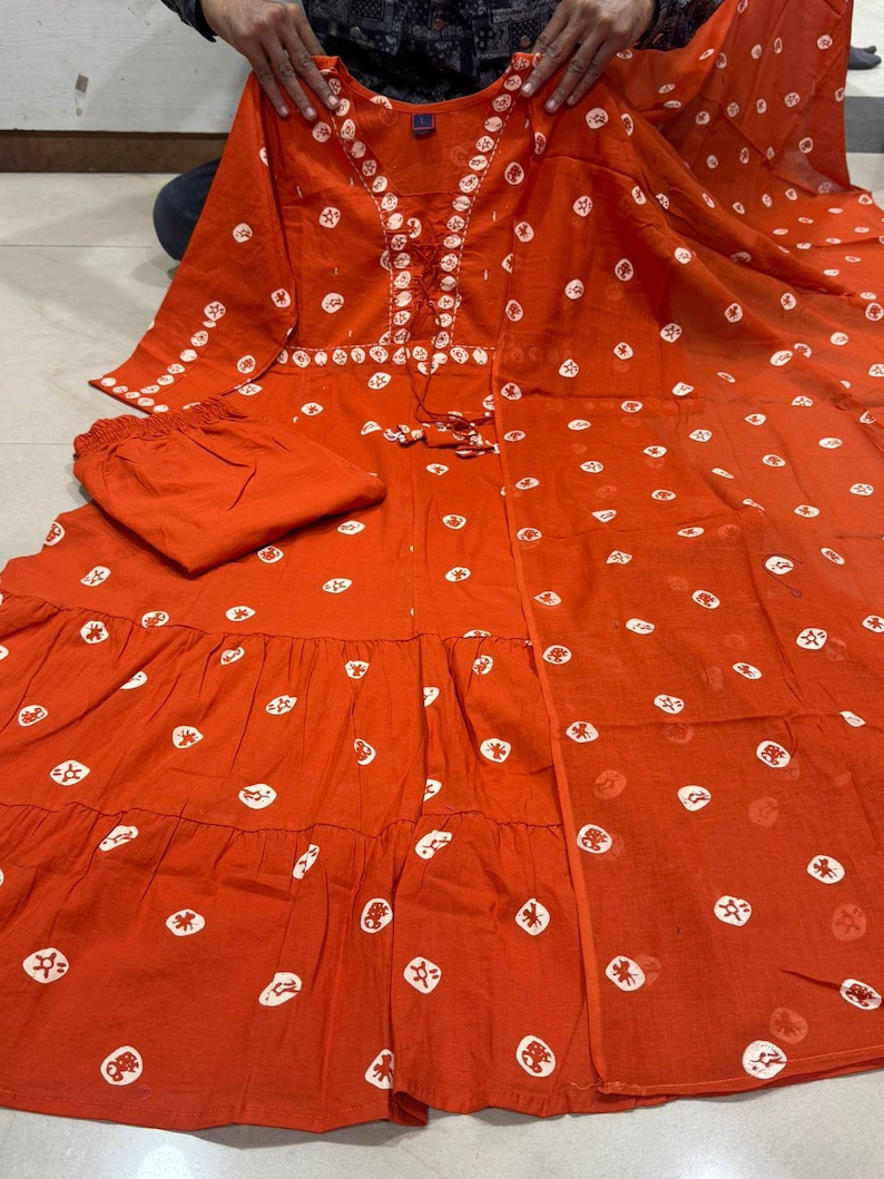 May include: A two-piece orange outfit with white polka dot patterns. The top has a V-neck with white embroidery and a drawstring. The outfit includes matching pants. The fabric appears to be lightweight.