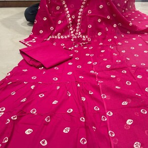 May include: A vibrant fuchsia-colored dress with a matching pair of pants. The dress features a tiered skirt and is adorned with white, circular patterns. The neckline is embellished with white embroidery. The outfit is made of a lightweight fabric.