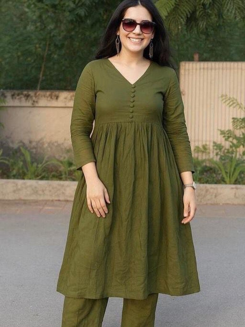 Peut inclure: Une robe vert olive &agrave; manches longues et col en V. La robe pr&eacute;sente un devant boutonn&eacute; et une taille fronc&eacute;e, associ&eacute;e &agrave; un pantalon assorti. La tenue est faite d'un tissu doux et fluide.