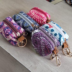 Puede incluir: Seis pequeños monederos con cremallera y estampados florales coloridos. Cada monedero tiene una cremallera dorada y una correa de cuero con un llavero dorado. Los monederos son en tonos rosa, morado, azul y blanco.