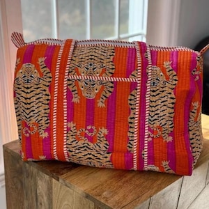Op de afbeelding: Een rechthoekige draagtas met een levendige tijgerprint. De tas heeft een herhalend patroon van tijgers op een achtergrond van verticale oranje en roze strepen. Witte randen accentueren de handvatten en randen.