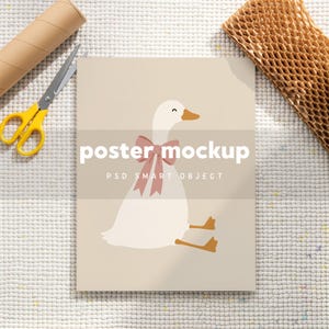 May include: A rectangular poster mockup featuring a light beige background with a central illustration of a white goose wearing a dusty pink bow. The text "poster mockup" and "PSD SMART OBJECT" is printed in white across the center of the goose.
