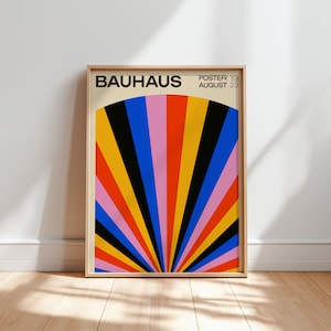 Op de afbeelding: Een ingelijste Bauhaus-poster met een levendig, geometrisch ontwerp. Het kunstwerk toont een waaiervormig patroon van kleurrijke strepen in rood, oranje, geel, zwart, blauw en roze. De poster bevat het woord "BAUHAUS" en de datum "POSTER 19 AUGUST 23".