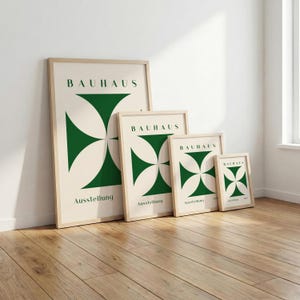 May include: Four framed Bauhaus art prints in varying sizes lean against a white wall. Each print features a green geometric design and the word "BAUHAUS" at the top. The word "Ausstellung" is printed at the bottom of each print.
