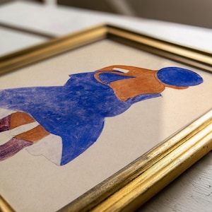 May include: A framed artwork featuring a figure in blue and orange. The artwork is in a gold frame, with the figure's form rendered in blue, orange, and purple hues. The artwork is on a cream-colored background.