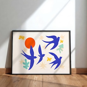 May include: A framed art print with a minimalist design. It features blue birds, an orange sun, yellow butterflies, and star shapes on a cream background. The artwork is framed in black and displayed on a wooden floor.