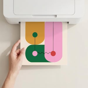 Puede incluir: Una impresora blanca está imprimiendo una colorida impresión de arte abstracto. La impresión presenta formas geométricas en amarillo mostaza, verde y rosa, con líneas negras y un fondo crema. Una mano sostiene la impresión.