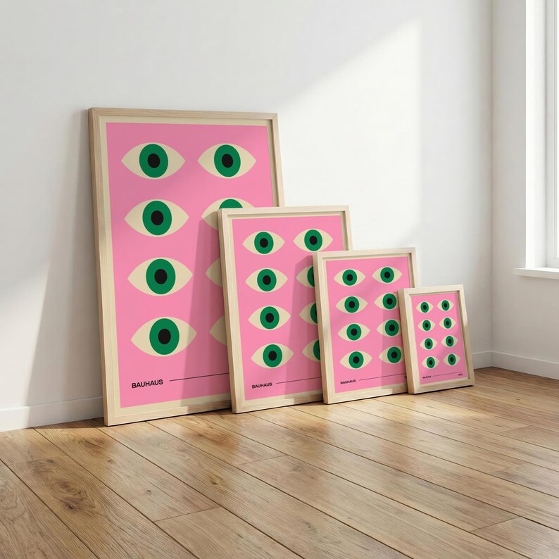 May include: Four framed art prints featuring a repeating eye design on a pink background. The eyes are green with off-white eyelids. The word "BAUHAUS" is printed at the bottom of the largest print. The frames are light wood.