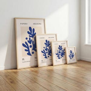 May include: A set of four framed art prints featuring a blue abstract design on a cream background. The prints are in varying sizes and have a light wood frame. Text includes "PAPIERS D&Eacute;COUP&Eacute;S" and "MATISS".