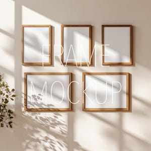 Könnte beinhalten: Fünf Holzbilderrahmen mit weißen Passepartouts sind an einer beigefarbenen Wand angebracht. Die Rahmen sind in einem Raster angeordnet. Der Text "FRAME MOCKUP" ist in Weiß über den Rahmen angeordnet. Die Szene wird von natürlichem Licht beleuchtet.