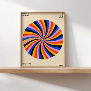 May include: A framed Bauhaus art print featuring a colorful spiral design in shades of red, orange, yellow, blue, and black. The print includes the text "BAUHAUS" and "1923" in a minimalist style. The artwork is displayed on a wooden shelf.