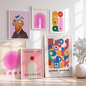 May include: A collection of framed Bauhaus art prints. The prints feature geometric shapes, abstract designs, and a portrait of a man with flowers and butterflies. The color palette includes pink, red, blue, yellow, and green. The prints are displayed on a white wall.